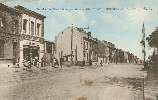 Vers 1950. Le passage à niveau est équipé de nouvelles barrières levées et abaissées manuellement. A gauche se trouve la librairie - papeterie - journaux propriété de Marcel Lechien et, derrière, la cour de l’Ouvroir, un établissement où était dispensé, fin XIXème siècle un enseignement religieux.

