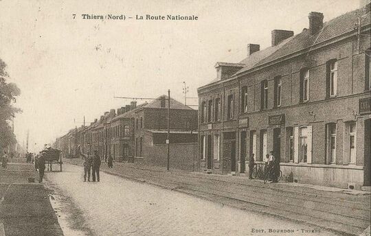 Vers 1930. A droite, les commerces se suivent depuis la place jusqu’à la S.O.C.O.M.A, à l’angle de la rue de la gare (rue Henri Legrand). Aujourd’hui, tout a disparu et vient d’être construit un immeuble composé de logements locatifs et de cellules commerciales au rez-de-chaussée.
