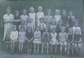 Photographie de groupe montrant plusieurs enfants accompagnés d’un adulte, probablement un enseignant, posant pour une photo de classe. Aucun texte ou élément graphique n’est visible sur l’image.