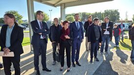 Un groupe de personnes (dont Madame La Maire) se tient à l’extérieur, sous un espace couvert. Elles portent des tenues formelles ou semi-formelles, ce qui laisse penser qu’elles participent à un événement ou un rassemblement officiel.
