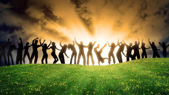 L’image montre un groupe de personnes en silhouette, debout sur un champ d’herbe parsemé de fleurs jaunes. Le ciel en arrière-plan est dramatique, avec des nuages et des rayons de soleil perçant à travers. Les personnes adoptent des poses dynamiques, évoquant le mouvement ou la célébration. Aucun détail facial ou vestimentaire n’est visible en raison de l’effet de silhouette.