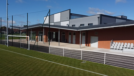 Photo de l'extérieure du complexe sportif côté terrain de foot avec une partie du terrain de foot